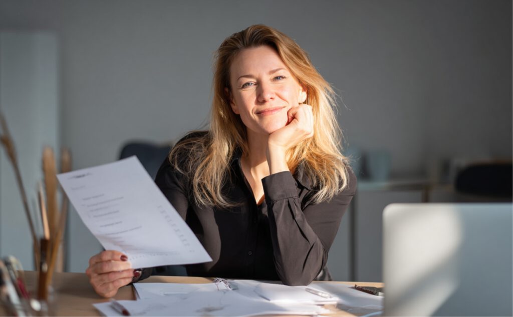 Frau am Schreibtisch mit Checkliste zur Steuerkanzlei-Wahl, Laptop und Notizbuch – ruhige, helle Büroszene bei Tageslicht