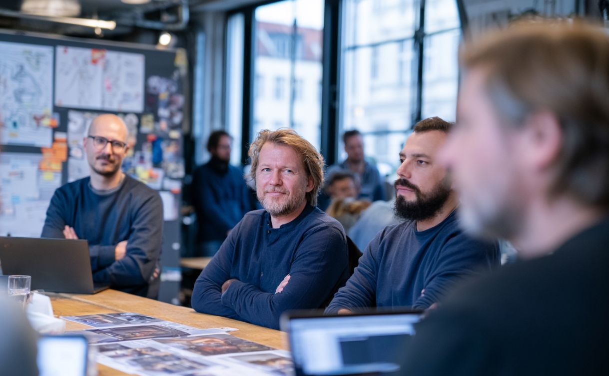 Kreativteam einer Berliner Agentur bespricht ein Projekt an einer Moodboard-Wand in einem hellen Altbau-Loft in Berlin Mitte, Laptops und Skizzen auf dem Tisch